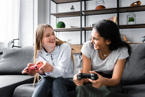 KYIV, UKRAINE - JULY 10, 2019: multicultural friends sitting on sofa and playing video game in apartment — Stock Photo