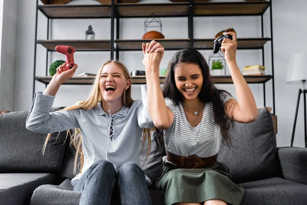 KYIV, UKRAINE - JULY 10, 2019: multicultural friends sitting on sofa and playing video game in apartment — Stock Photo