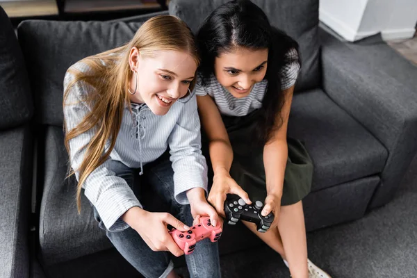 KYIV, UKRAINE - JULY 10, 2019: high angle view of multicultural friends sitting on sofa and playing video game in apartment — Stock Photo