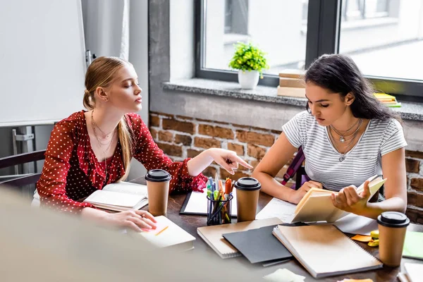 Amigos multiculturais atraentes sentados à mesa e estudando em apartamento — Fotografia de Stock