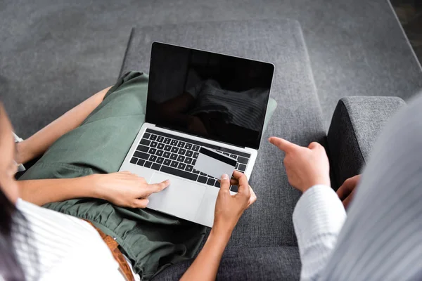 Cropped view of multicultural friends holding credit card and using laptop in apartment — Stock Photo