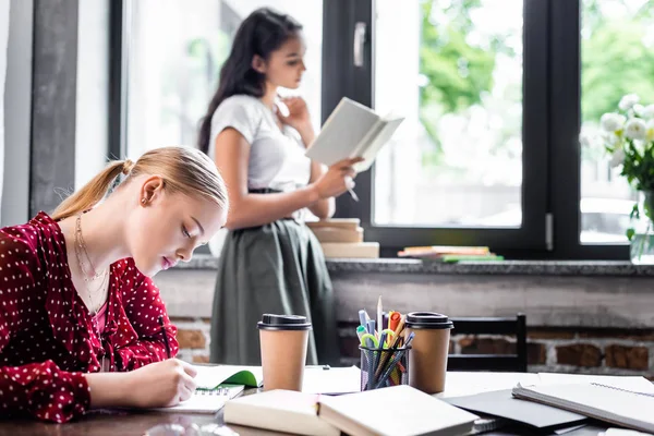 Selective focus of attractive student in blouse writing in apartment — Stock Photo