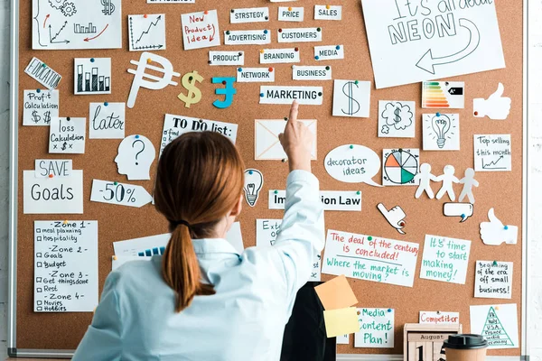 Back view of businesswoman pointing with finger at marketing lettering on notice board — Stock Photo