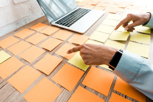 Cropped view of woman pointing with finger at sticky notes near laptop with blank screen — Stock Photo