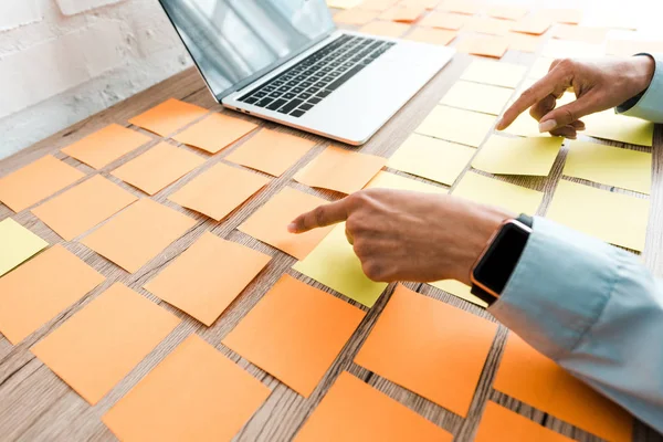 Cropped view of woman pointing with finger at sticky notes near laptop with blank screen — Stock Photo