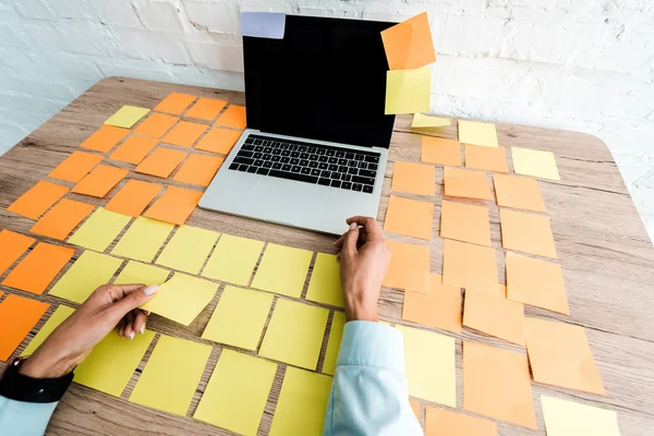 Vue recadrée de la femme près de notes collantes et ordinateur portable avec écran blanc sur le bureau — Photo de stock