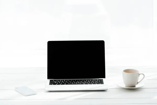 Smartphone in der Nähe von Tasse Kaffee und Laptop mit leerem Bildschirm auf weiß — Stockfoto