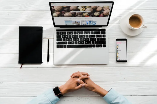 KYIV, UKRAINE - JULY 23, 2019: top view of woman with clenched hands near laptop with depositphotos website and smartphone with apple music app on screen — Stock Photo