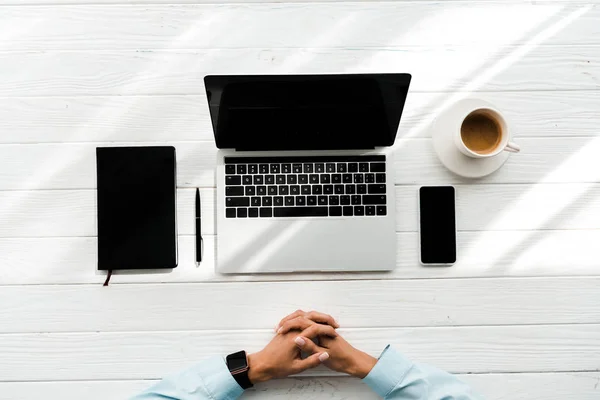 Vue du dessus de la femme assise avec les mains serrées près de l'ordinateur portable et tasse avec café — Photo de stock