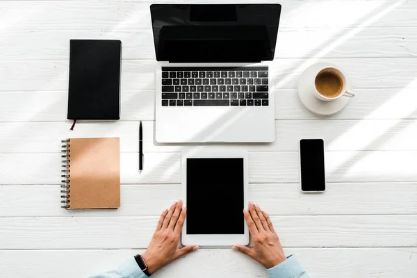 Vista superior de la mujer sosteniendo la tableta digital cerca de gadgets y taza con café - foto de stock