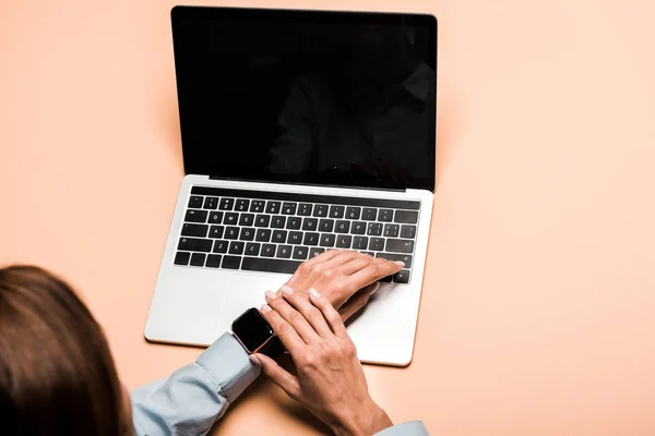 Vista recortada de la mujer tocando reloj inteligente cerca de la computadora portátil con pantalla en blanco en rosa - foto de stock