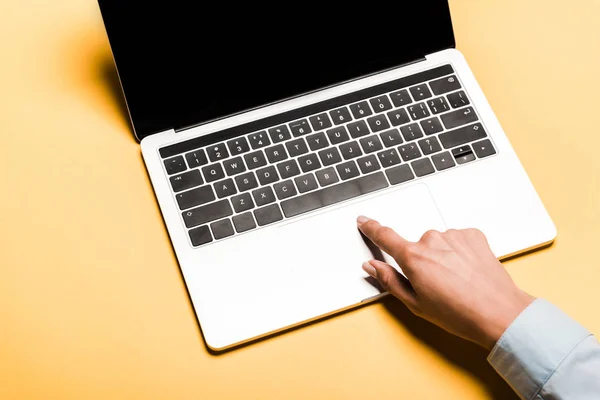 Cropped view of woman using laptop with blank screen on orange — Stock Photo