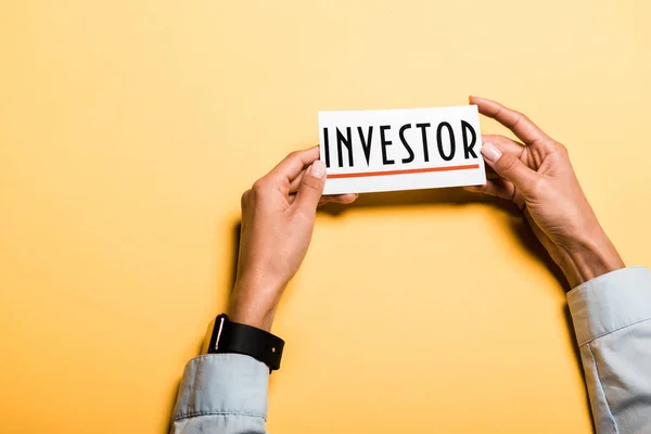 Top view of girl holding card with investor lettering on orange — Stock Photo