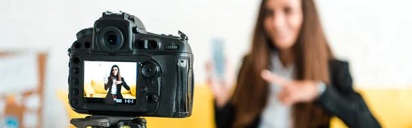 Fotografía panorámica de la cámara digital con el vídeo blogger feliz apuntando con el dedo al teléfono inteligente - foto de stock