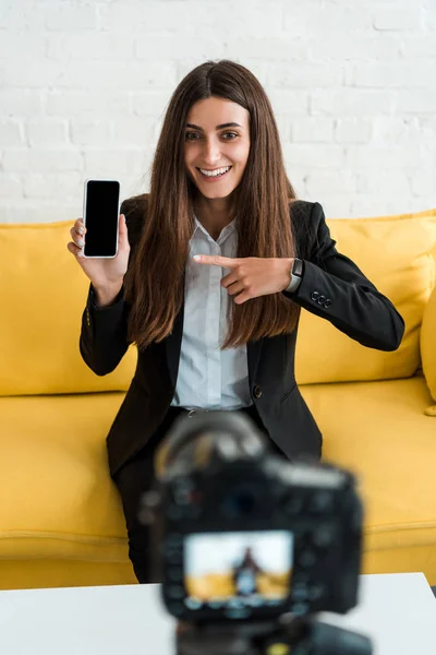 Messa a fuoco selettiva di donna felice che punta con il dito allo smartphone con schermo bianco vicino alla fotocamera digitale — Foto stock