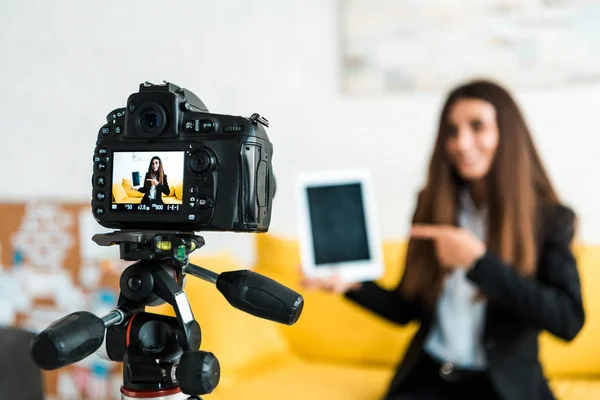 Foco seletivo da câmera digital com blogueiro de vídeo feliz apontando com o dedo para tablet digital com tela em branco — Stock Photo