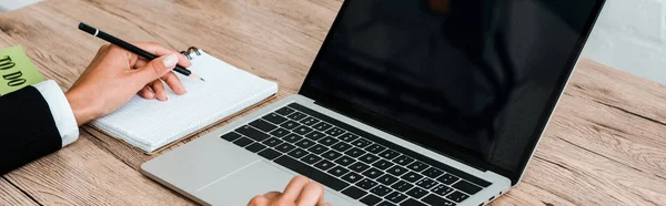 Tiro panorâmico de mulher segurando caneta ao usar laptop com tela em branco — Fotografia de Stock