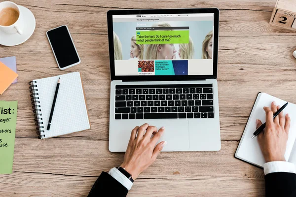 KYIV, UKRAINE - JULY 23, 2019: top view of woman using laptop with bbc website near smartphone with blank screen — Stock Photo