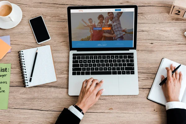 KYIV, UKRAINE - JULY 23, 2019: top view of woman using laptop with couchsurfing website near smartphone with blank screen — Stock Photo