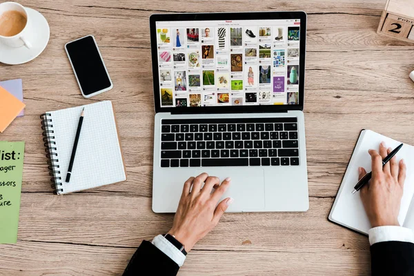 KYIV, UKRAINE - JULY 23, 2019: top view of woman using laptop with pinterest website near smartphone with blank screen — Stock Photo