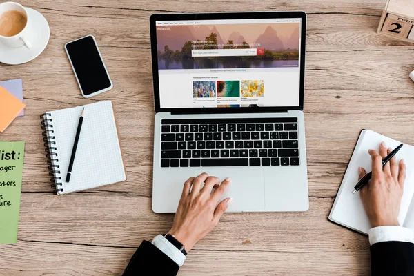 KYIV, UKRAINE - JULY 23, 2019: top view of woman using laptop with shutterstock website near smartphone with blank screen — Stock Photo