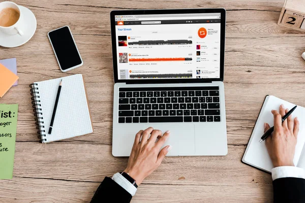 KYIV, UKRAINE - JULY 23, 2019: top view of woman using laptop with soundcloud  website near smartphone with blank screen — Stock Photo