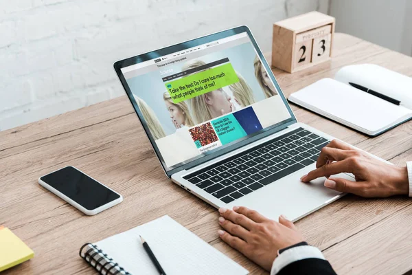 KYIV, UKRAINE - JULY 23, 2019: cropped view of woman using laptop with bbc website near smartphone with blank screen and wooden cubes — Stock Photo