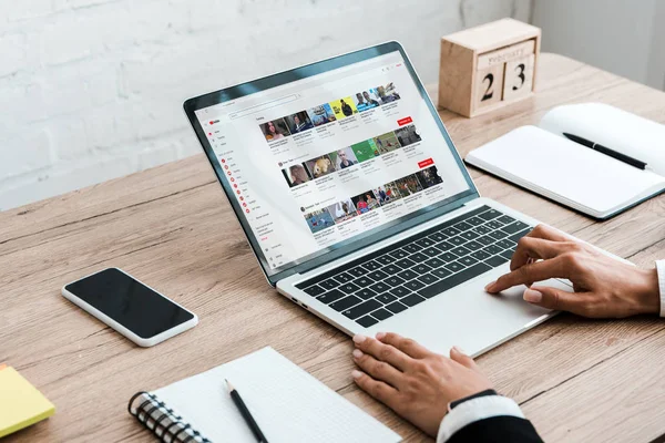 KYIV, UKRAINE - JULY 23, 2019: cropped view of woman using laptop with youtube website near smartphone with blank screen and wooden cubes — Stock Photo