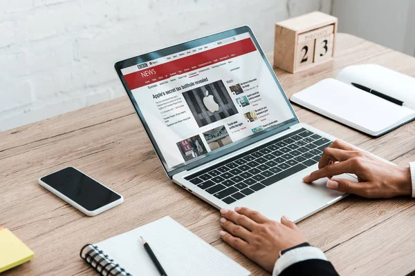 KYIV, UKRAINE - JULY 23, 2019: cropped view of woman using laptop with bbc news website near smartphone with blank screen and wooden cubes — Stock Photo