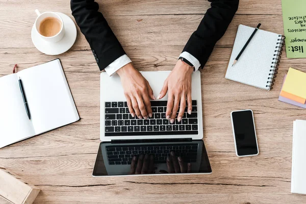 Vista dall'alto di donna d'affari che digita su computer portatile vicino a tazza di caffè in ufficio — Foto stock