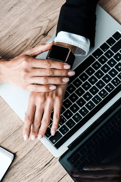 Ansicht von oben: Frau berührt Smart Watch in der Nähe von Laptop — Stockfoto