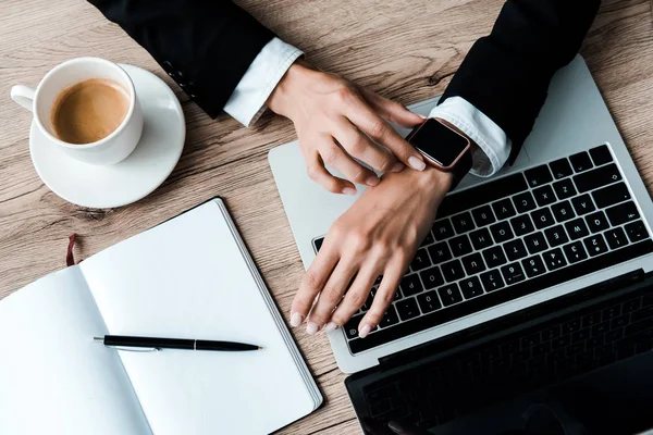 Vista superior de la mujer tocando reloj inteligente cerca del ordenador portátil y la taza de café - foto de stock