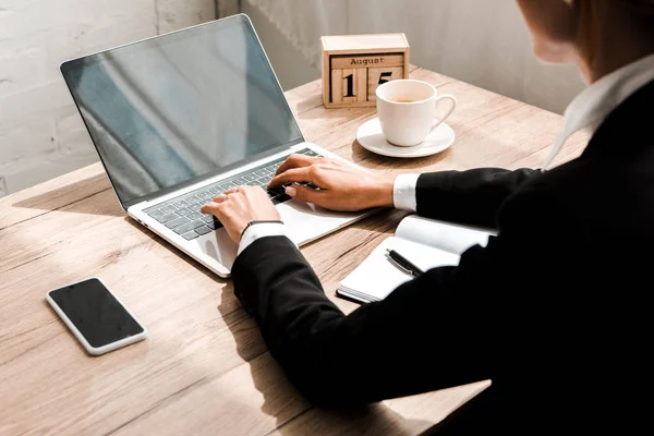 Foco seletivo da mulher digitando no laptop perto de cubos de madeira com calendário e smartphone com tela em branco — Fotografia de Stock