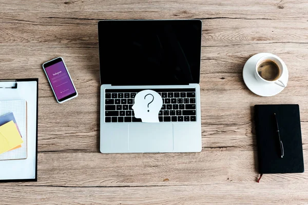 KYIV, UKRAINE - JULY 23, 2019: top view of smartphone with instagram app near laptop with blank screen and paper human head with question mark — Stock Photo