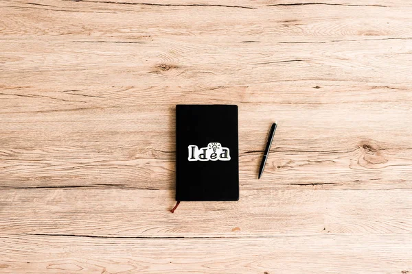 Top view of paper with idea lettering on black notebook with pen — Stock Photo