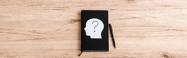 Panoramic shot of paper human head with question mark on black notebook near pen — Stock Photo