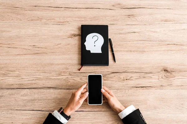 Top view of woman holding smartphone with blank screen near notebook and paper human head with question mark — Stock Photo