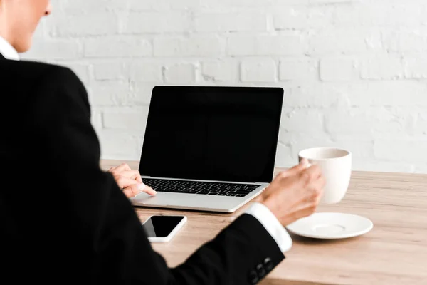 Selective focus of woman holding cup while sitting near gadgets in office — Stock Photo