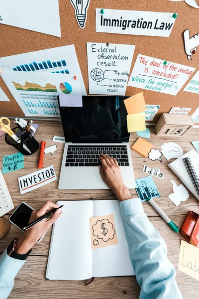 Vista superior de la mujer de negocios que sostiene la pluma cerca del cuaderno y gadgets con pantallas en blanco - foto de stock