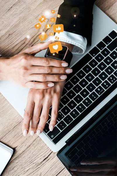 Top view of woman touching smart watch with orange speech bubbles with signs near laptop — стоковое фото