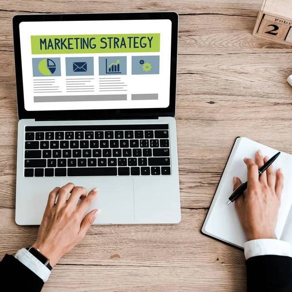 Top view of woman holding pen while using laptop with marketing strategy lettering on screen — Stock Photo