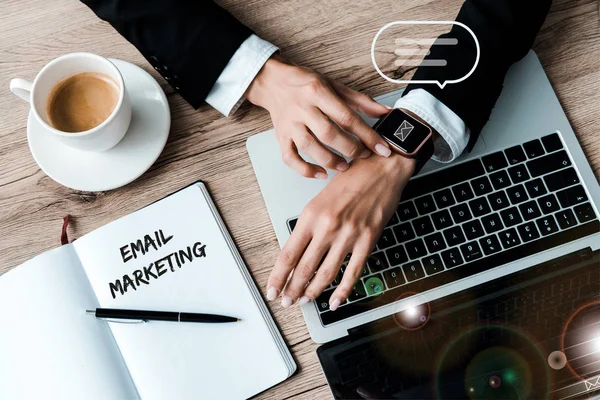 Vista superior da mulher tocando relógio inteligente com envelope perto de laptop e xícara de café — Fotografia de Stock