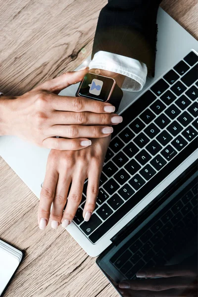 Vista dall'alto della donna che tocca orologio intelligente con i social media vicino al computer portatile — Foto stock