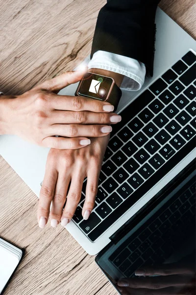 Vista superior de la mujer tocando reloj inteligente con sobre cerca del ordenador portátil - foto de stock