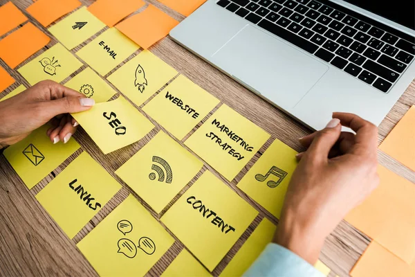 Cropped view of woman touching sticky note with seo lettering near laptop on desk — Stock Photo