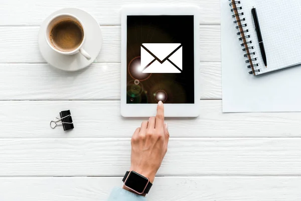 Ansicht von oben: Frau zeigt mit dem Finger auf digitales Tablet mit Umschlag auf dem Bildschirm in der Nähe von Kaffeetasse und Büroklammer — Stockfoto