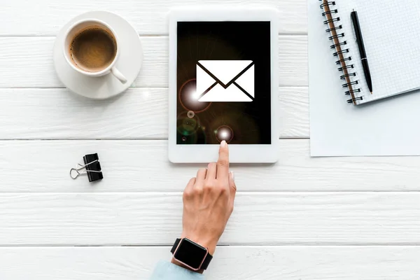 Top view of woman pointing with finger at digital tablet with envelope on screen near cup of coffee and paper clip — Stock Photo