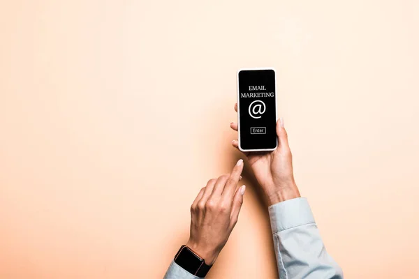 Cropped view of woman pointing with finger at smartphone with email marketing lettering on pink — Stock Photo