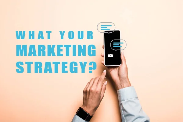 Cropped view of woman pointing with finger at smartphone with what your marketing strategy lettering on pink — Stock Photo