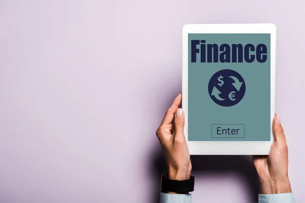Обрезанный вид женщины, держащей цифровой планшет с финансовыми надписями на фиолетовом — стоковое фото